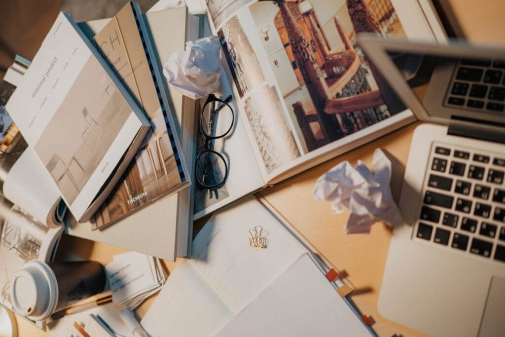 The Back-Office Chaos Trap and 5 Steps to Escape It 2 A cluttered desk with books, eyeglasses, crumpled papers, and a laptop, representing the back-office chaos trap that overwhelms service-based business owners